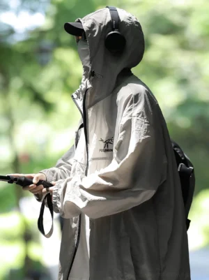 Light gray hooded sun protection jacket shown in side profile on an outdoor forest trail with adjustable hood, oversized fit, backpack, headphones, and hiking styling