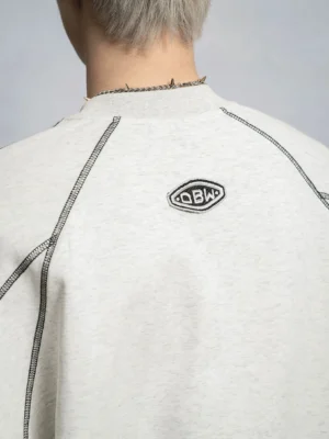 Close up back view of a light gray oversized contrast stitch sweatshirt showing bold black seam detailing, embroidered back patch, and soft fleece touch fabric