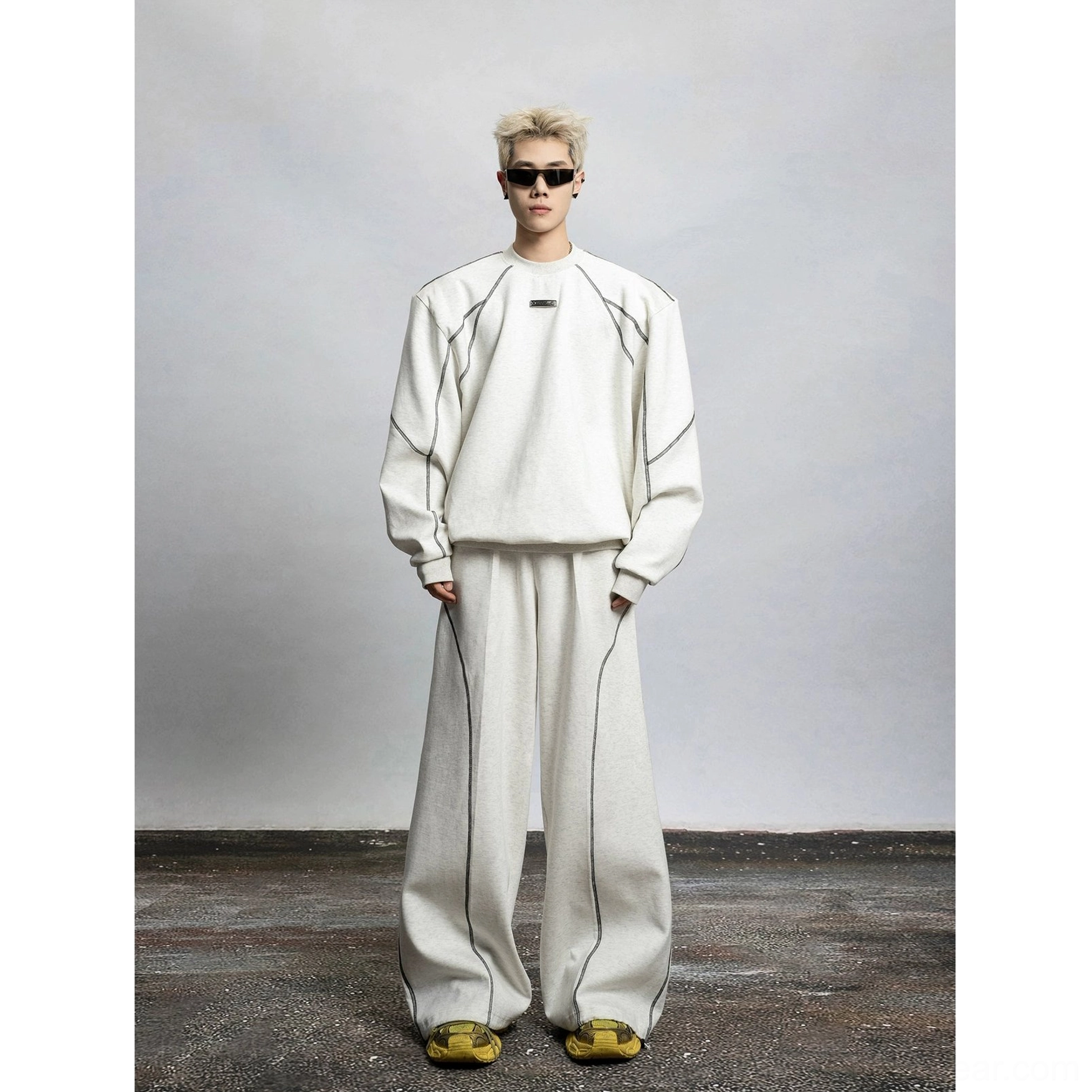 Full front view of a light gray oversized contrast stitch sweatshirt with silver topstitching, chest panel detail, and matching neutral wide leg trousers
