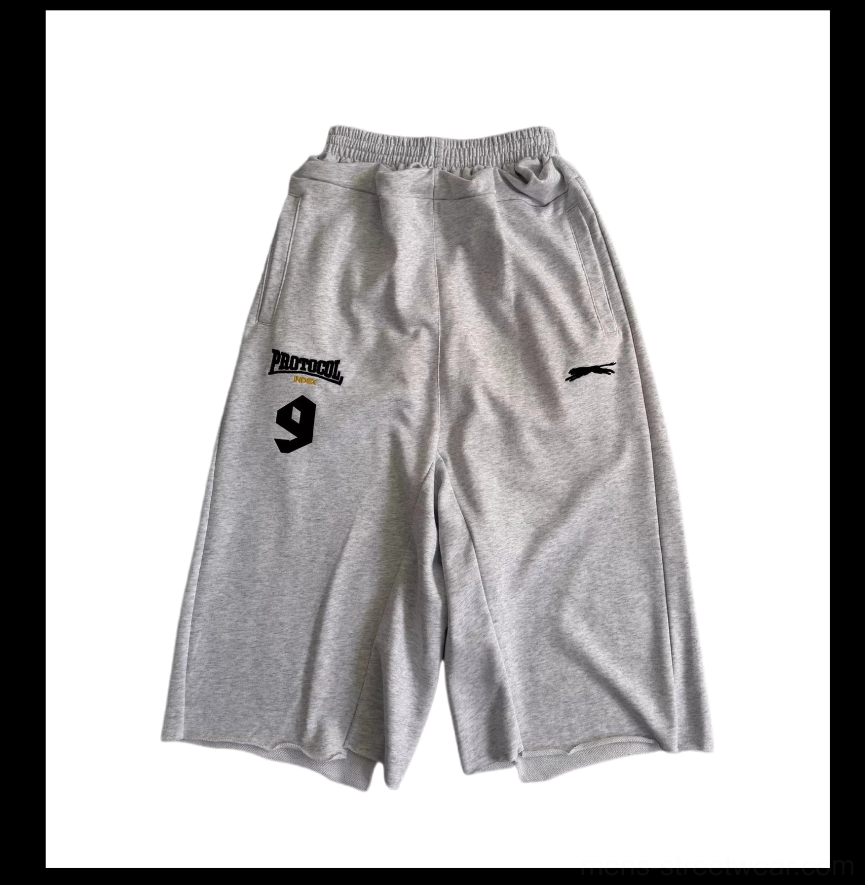 Flat lay front view of light gray oversized 7/8 court shorts with elastic waistband, wide-leg cut, and PROTOCOL 9 thigh graphic