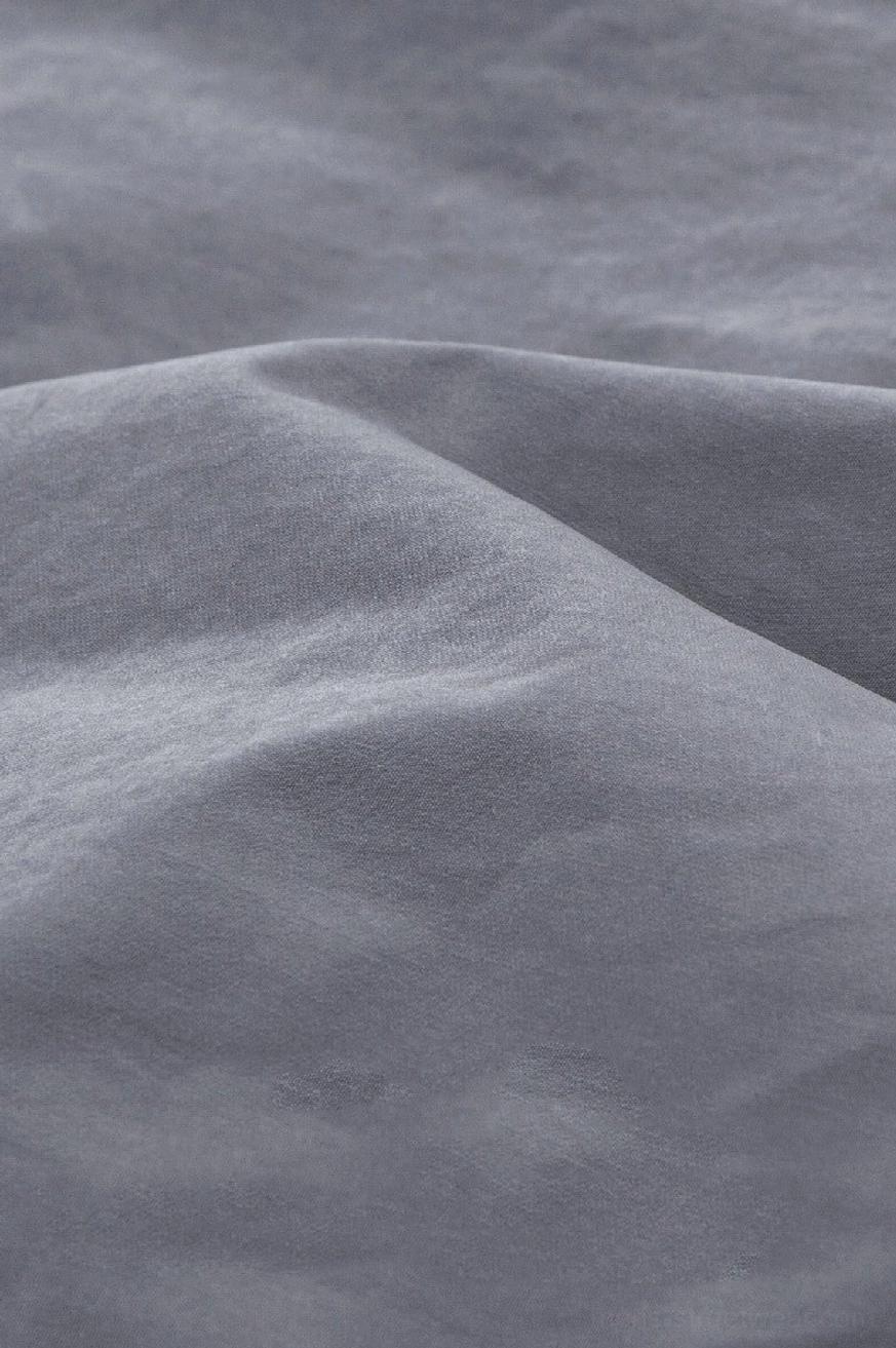 Close-up of smooth matte light gray woven fabric used on oversized streetwear windbreaker jacket