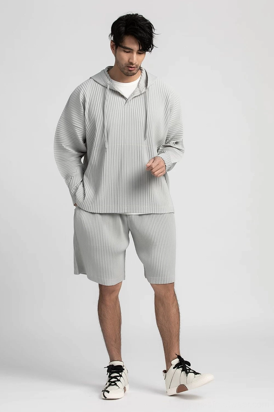 Light gray pleated tech shorts styled with a matching drawstring hoodie in a relaxed outfit