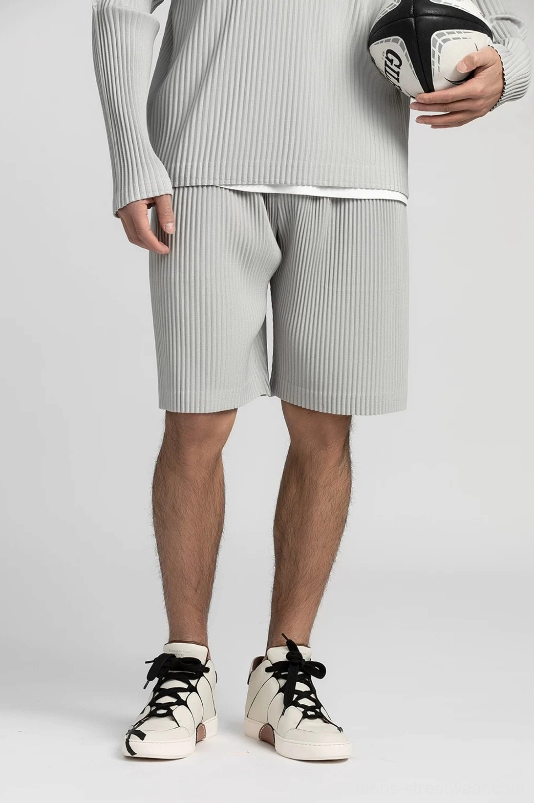 Light gray pleated tech shorts with matching long sleeve top and two tone sneakers in a studio setting