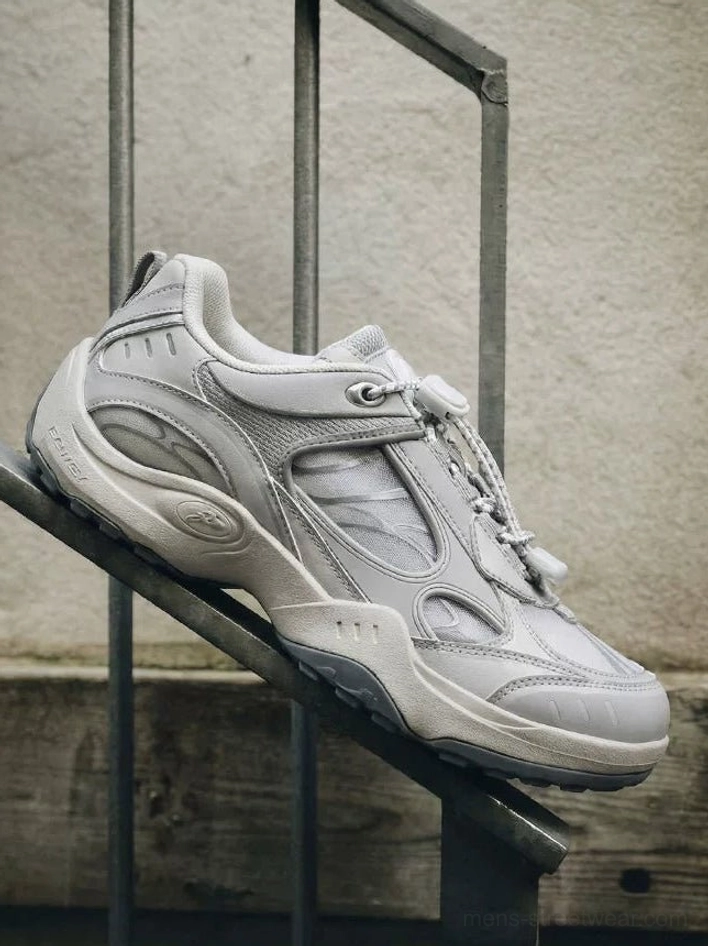 Light grey retro techwear sneakers with breathable mesh panels, bungee toggle fastening, chunky rubber outsole, and urban industrial stairway styling