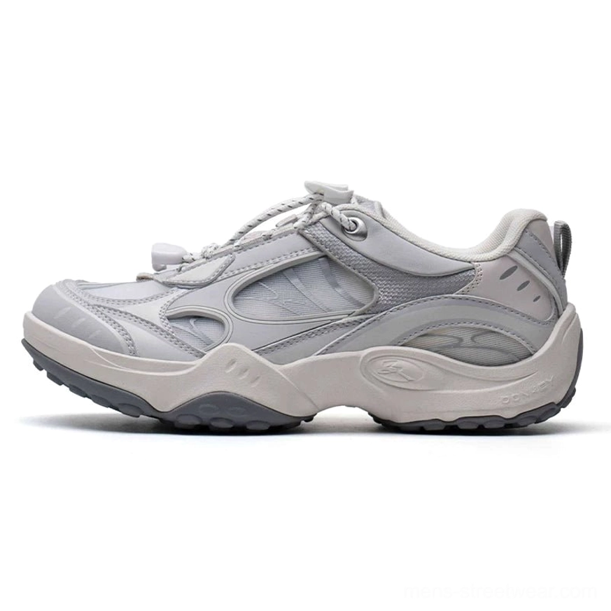Light grey techwear runner sneakers with layered mesh and suede-style panels, bungee toggle laces, heel pull tab, and chunky rubber outsole on a white background