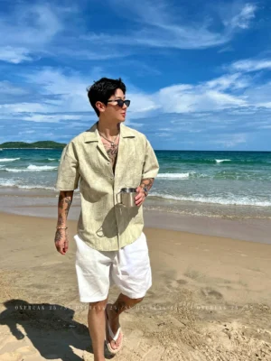 Light Khaki washed seersucker Cuban collar short sleeve shirt styled with white shorts and sandals on a sandy beach