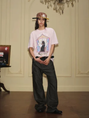 Female model wearing a light pink winged cat graphic T-shirt with dark wide leg jeans in vintage streetwear styling