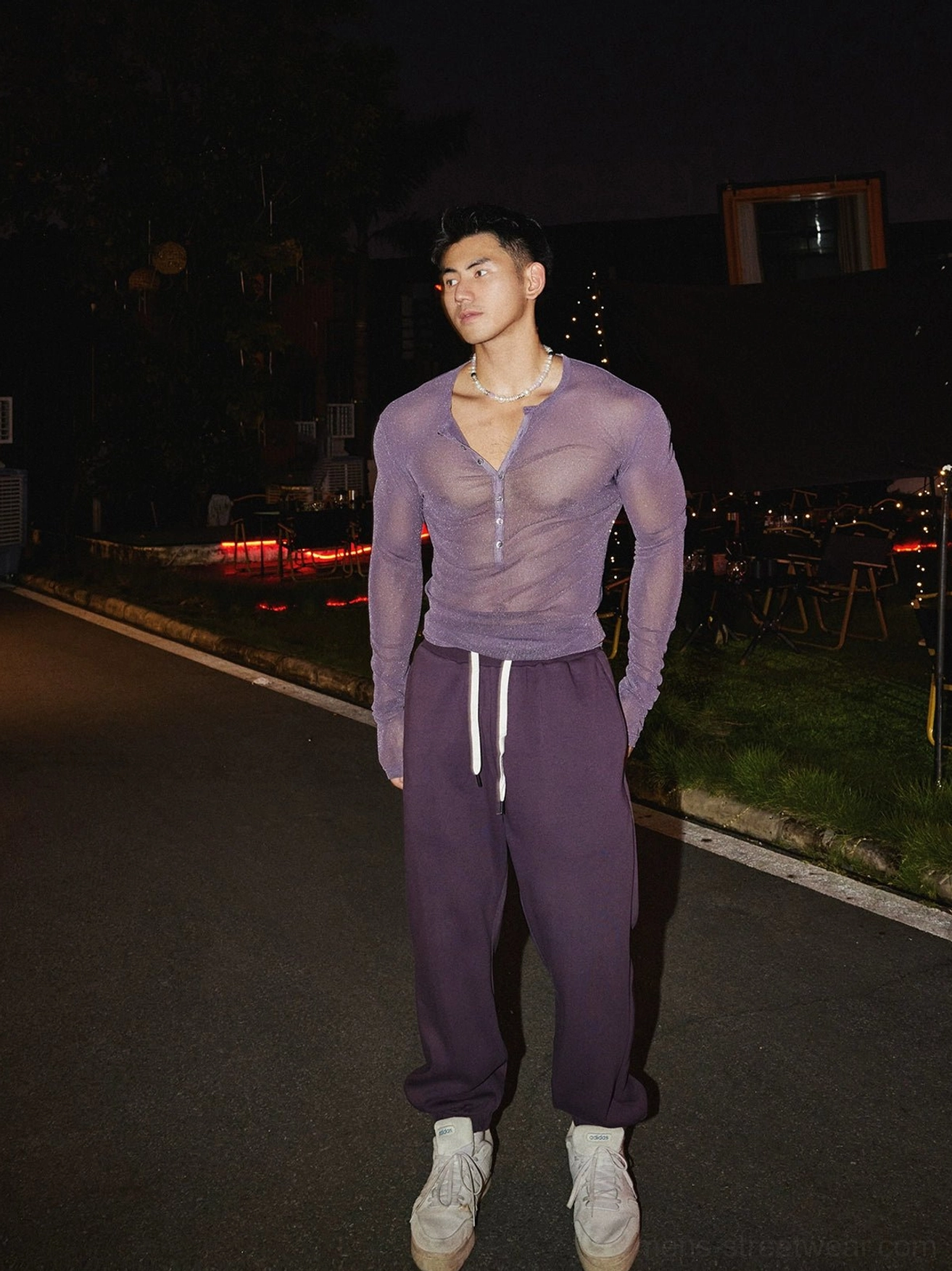 Rear-side full-length view of a male model wearing a light purple sheer sparkly long sleeve Henley top with purple sweatpants
