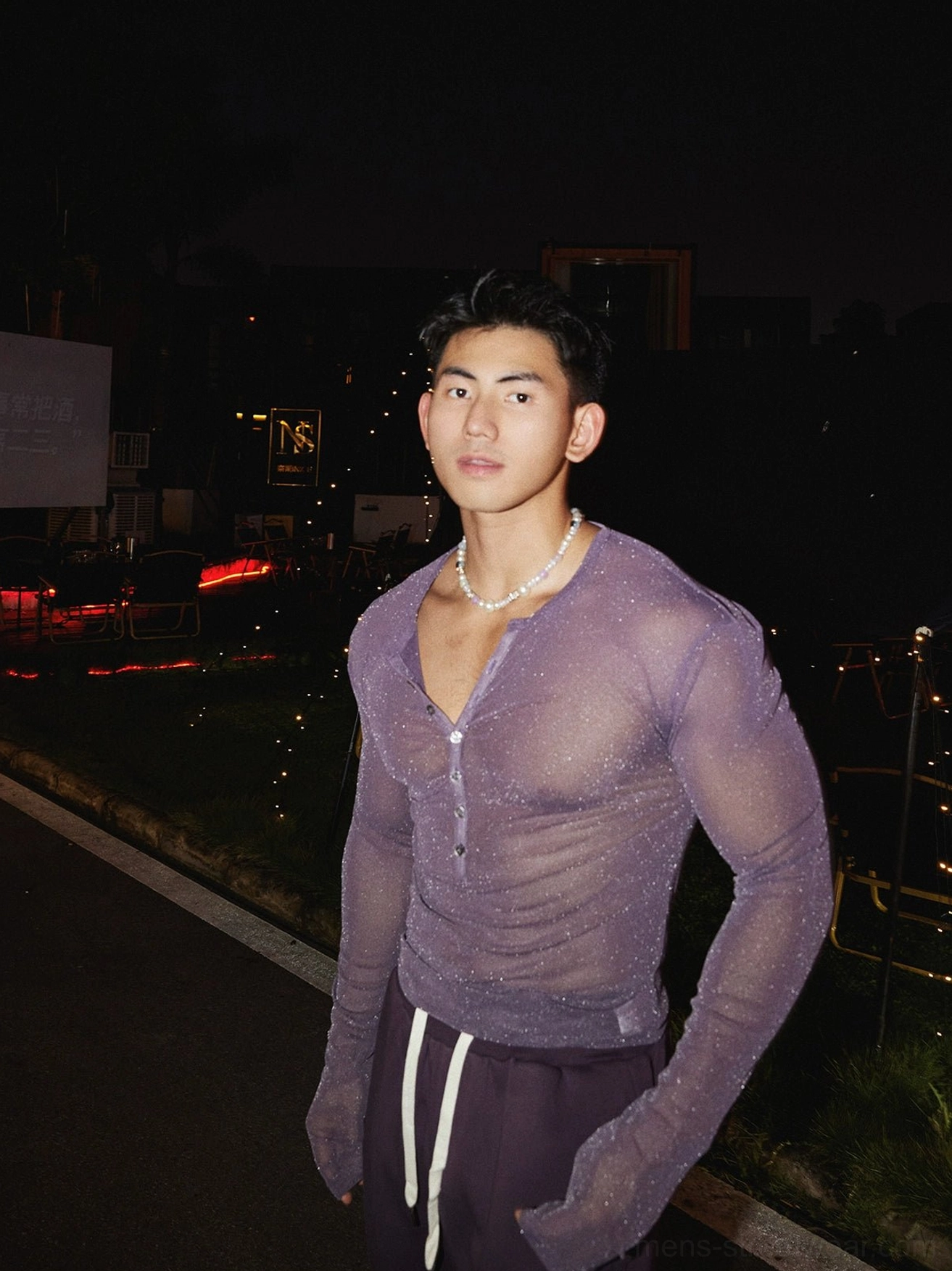 Full-length front view of a male model wearing a light purple sheer sparkly Henley long sleeve top with drawstring sweatpants