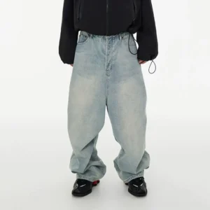 Front view of light wash balloon fit jeans with ultra-baggy wide legs, dropped crotch, faded blue denim, and stacked hems styled with a black cropped jacket