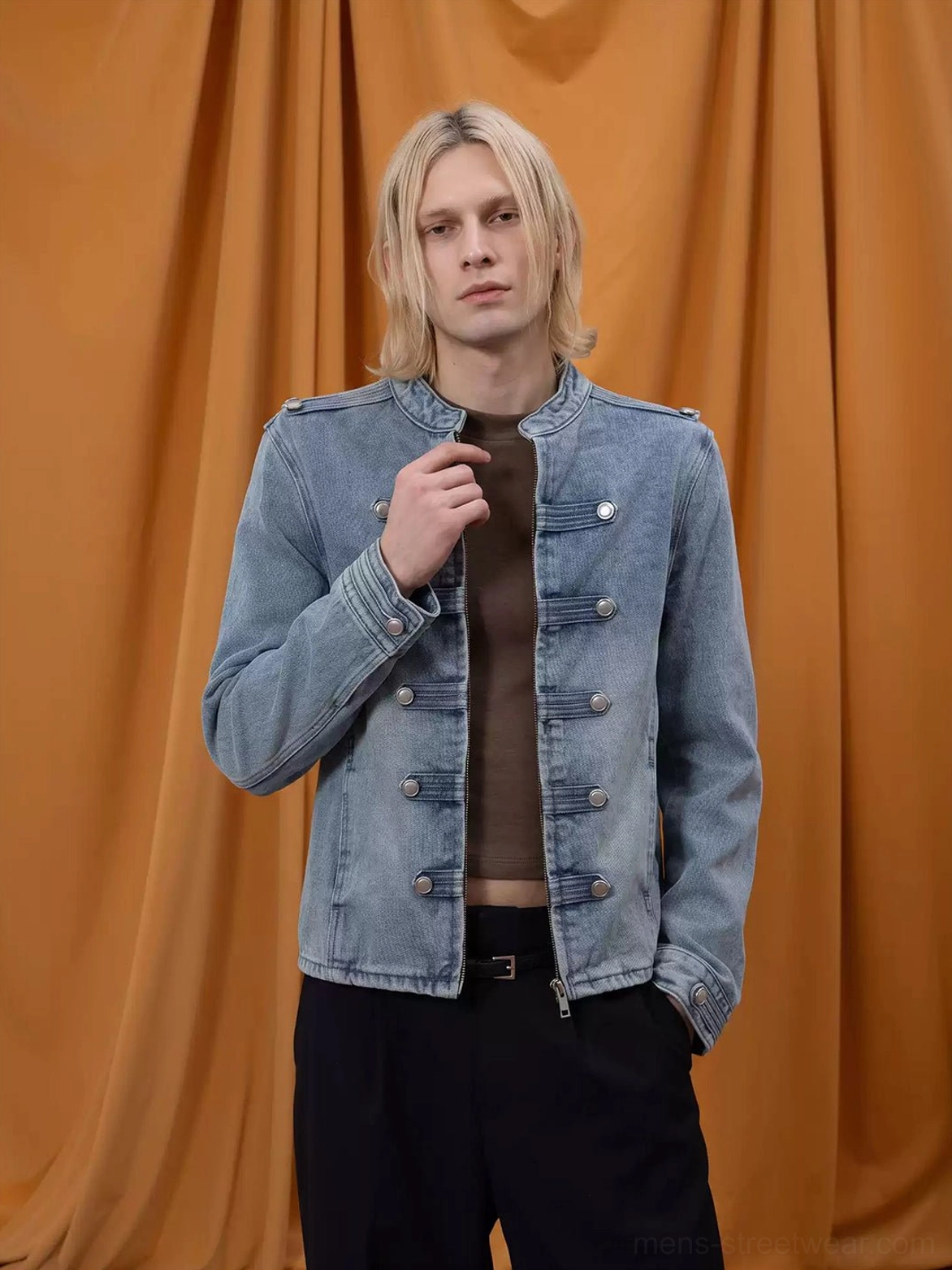 Front view of male model styling a light wash denim military cropped jacket with stand collar and buttoned cuffs