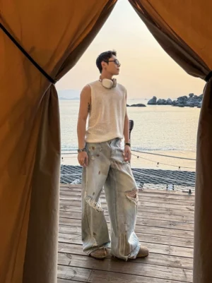 Male model wearing light blue heavy distressed wide leg denim jeans with ripped knees and vintage washed streetwear finish