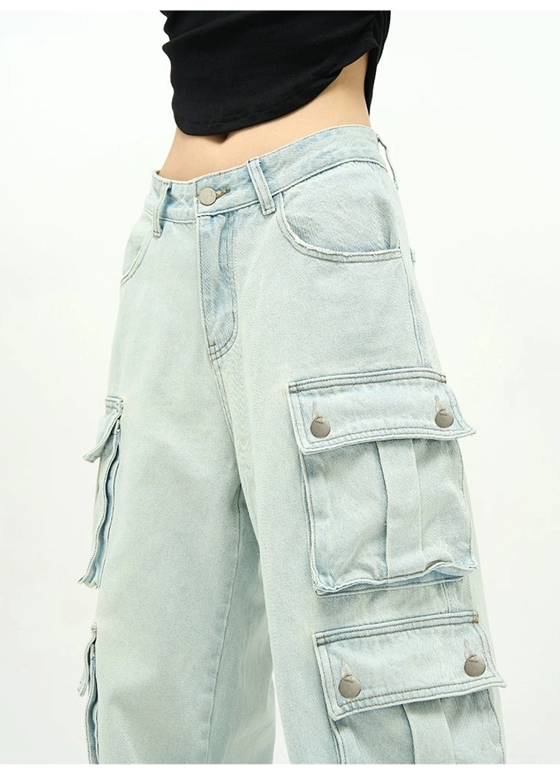 Close-up of light washed denim cargo jeans showing button-secured flap pocket, waistband stitching, utility details, and wide-leg construction