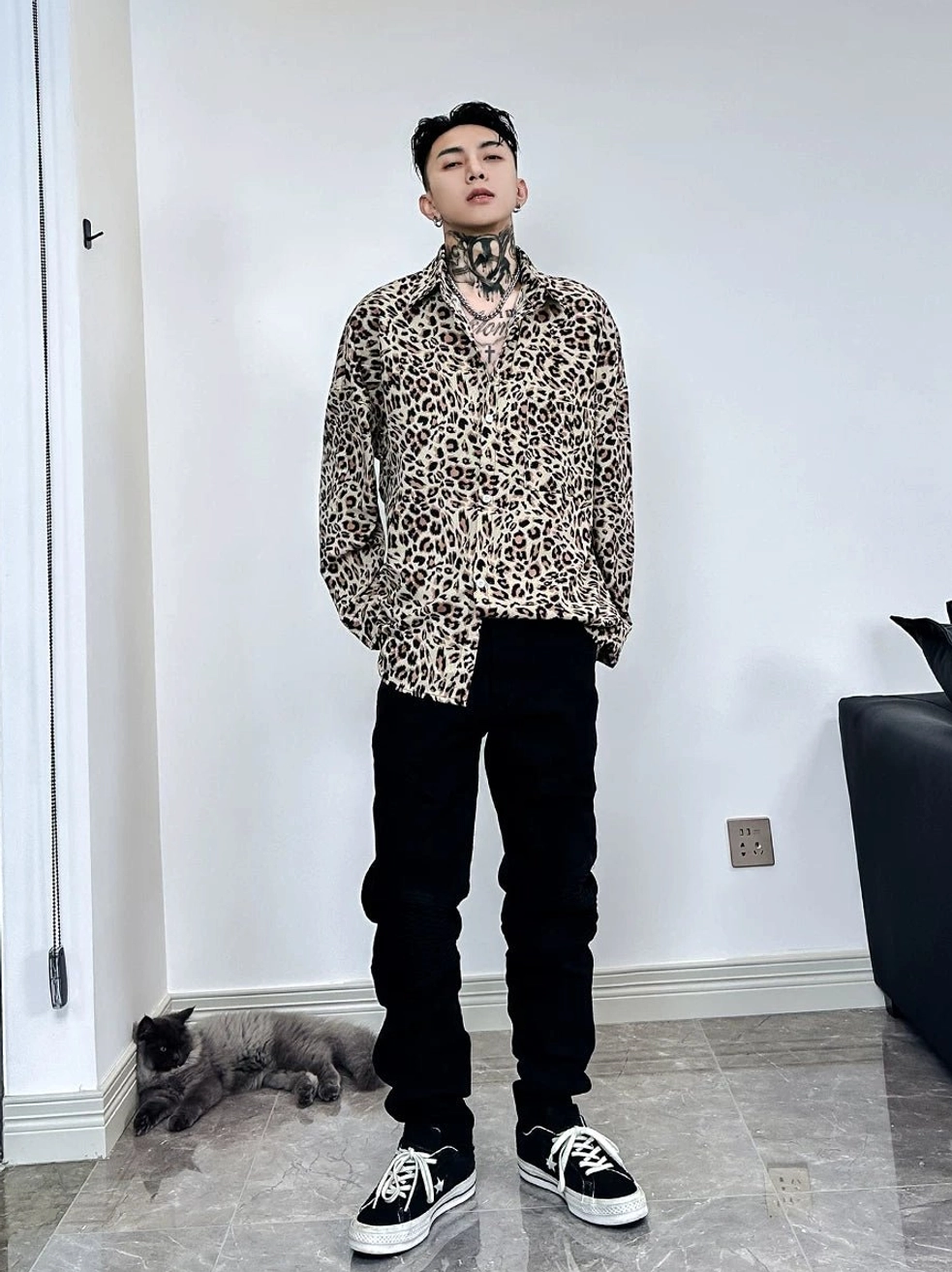 Front view of a male model wearing a long-sleeve leopard print satin shirt partially tucked into high-waisted black trousers