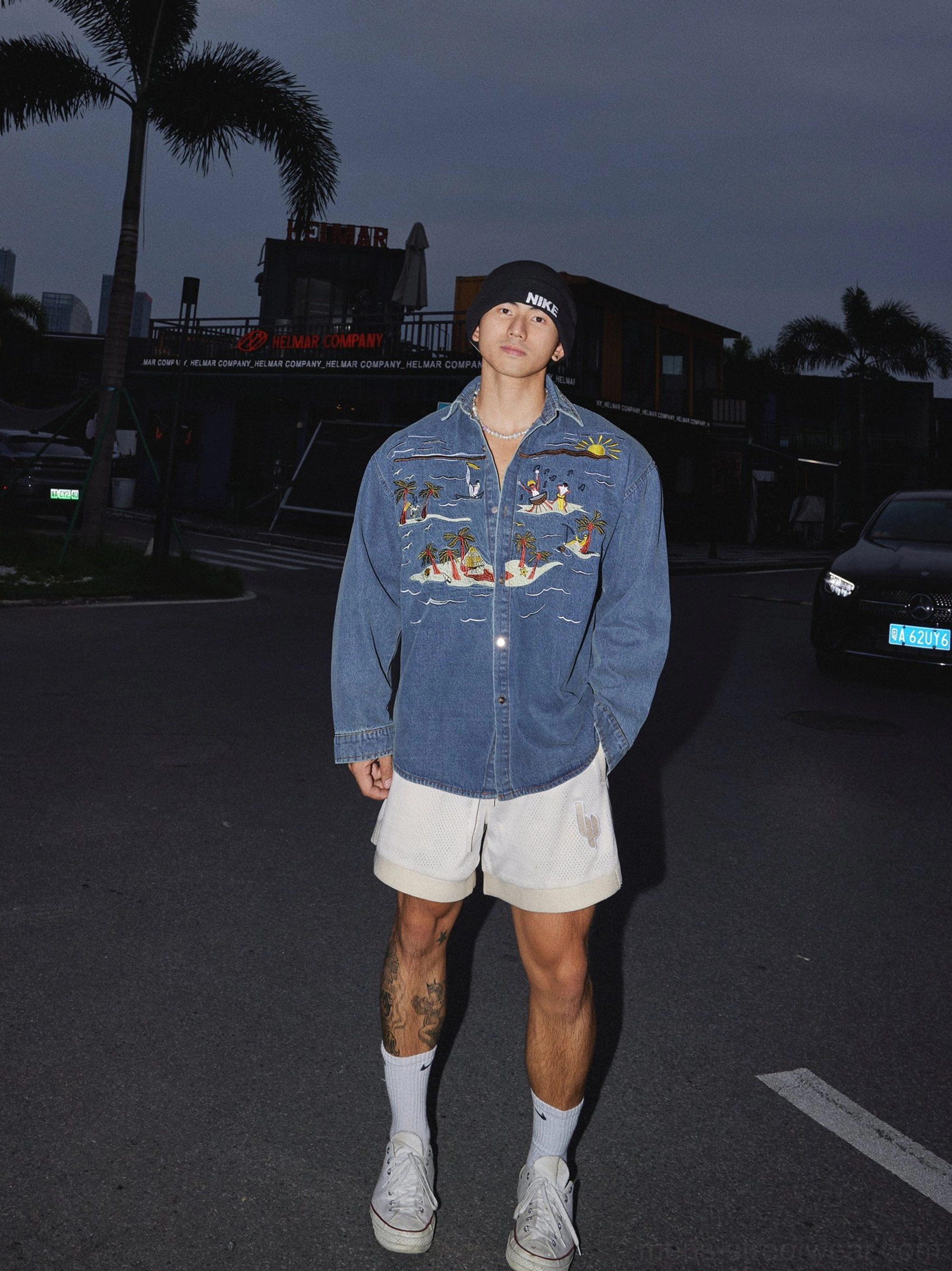 Long sleeve tropical embroidered denim shirt in washed indigo with palm tree sunset artwork styled with shorts and canvas sneakers