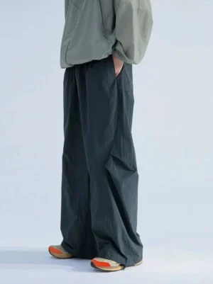 Side view of loose pleated wide-leg track pants with crinkled woven texture, side pockets, and adjustable drawstring hems styled in Korean streetwear