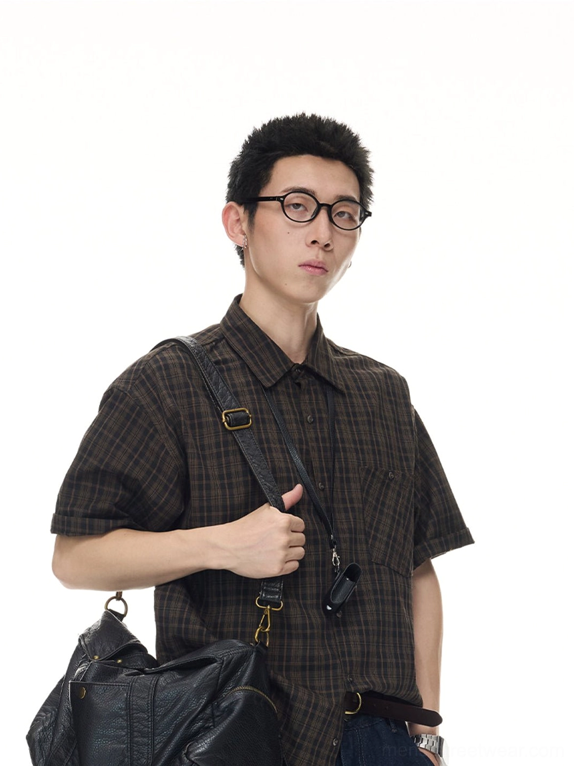 Male model wearing a coffee brown vintage plaid short sleeve button shirt with dark wide leg jeans, leather bag, and work badge