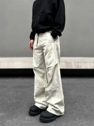Front three quarter view of off white marble wash wide leg cargo pants with dimensional panel seams and metal waist chain in an urban streetwear setting
