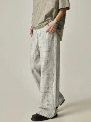 Marbled grey wide-leg jeans shown from a left three-quarter angle with an oversized grey T-shirt and black loafers in a minimalist studio streetwear outfit