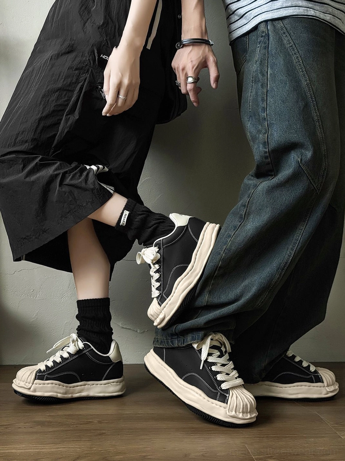 Two people wearing matching black and cream distressed shell-toe platform sneakers in coordinated streetwear outfits