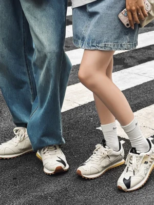 Matching ivory retro runner sneakers worn with white crew socks and denim outfits on an urban crosswalk
