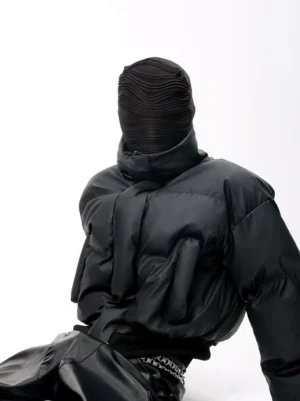Matte black cropped puffer jacket shown from a three-quarter rear view with high stand collar, quilted padding, relaxed sleeves, and ribbed hem in a monochrome streetwear outfit