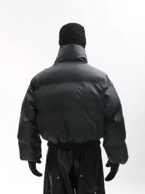 Rear view of a matte black cropped puffer jacket featuring a padded quilted silhouette, relaxed long sleeves, high collar, and solid black technical streetwear design