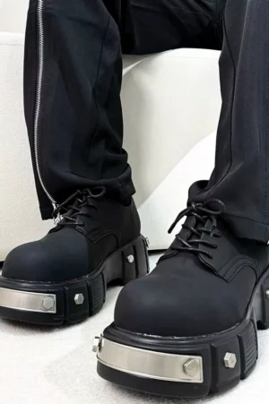 Matte black metal platform Derby shoes worn with black zippered straight-leg trousers, featuring a thick lug sole and silver hardware for gothic streetwear styling