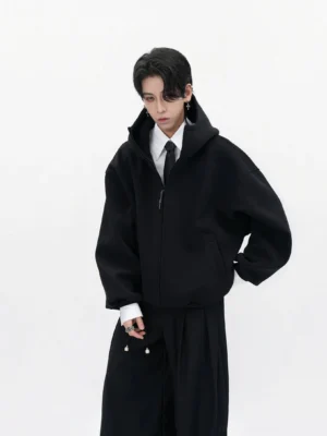 Matte black oversized high-neck zip-up hoodie with relaxed dropped shoulders styled over formal shirt and wide-leg black pants