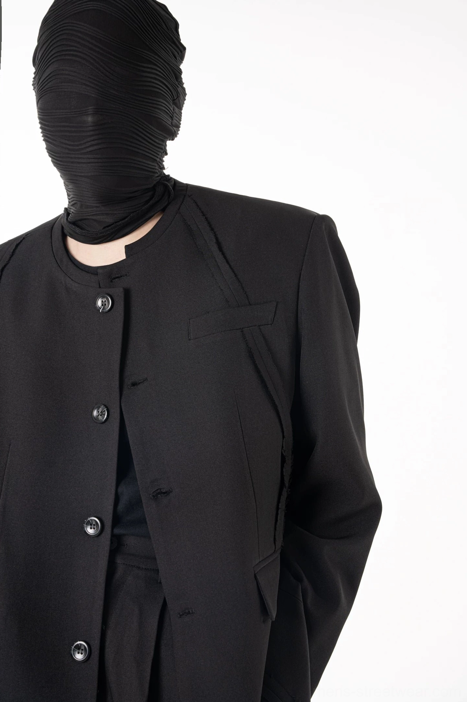 Close-up front view of matte black tailored blazer with five visible buttons chest pocket and architectural seam details