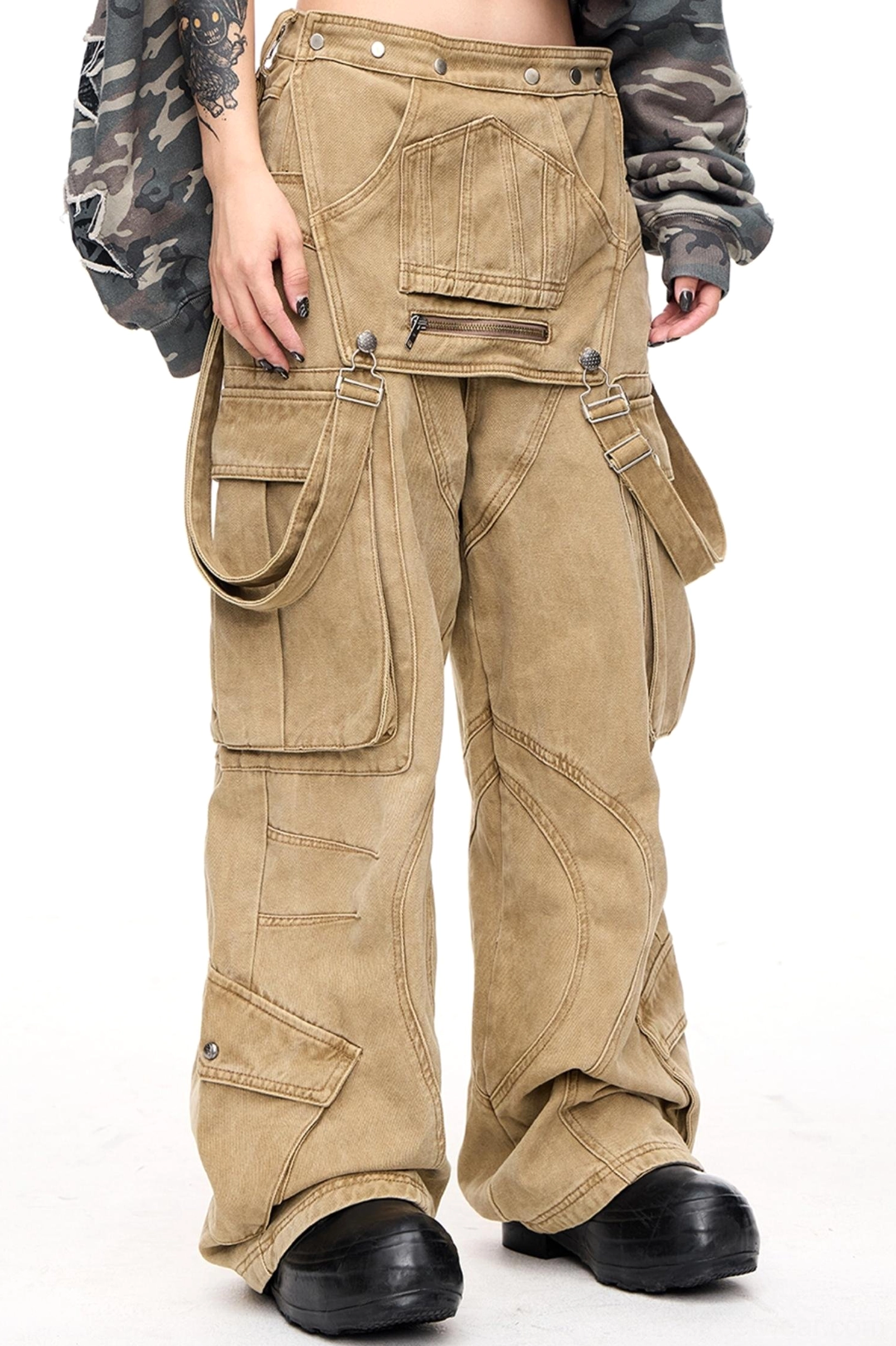 Side front view of men's apricot cargo pants with visible thigh pockets, detachable front panel straps, curved stitching, and wide-leg streetwear silhouette