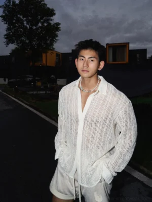 Men's apricot long-sleeve open-knit crochet shirt styled with beige drawstring shorts in a relaxed streetwear outfit