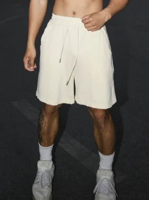 Men's apricot raw hem drawstring sweat shorts in a relaxed knee-length streetwear fit shown on a model at night