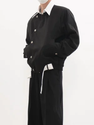 Black asymmetric button cropped blouson jacket worn with a white collared shirt and black wide-leg trousers in a studio