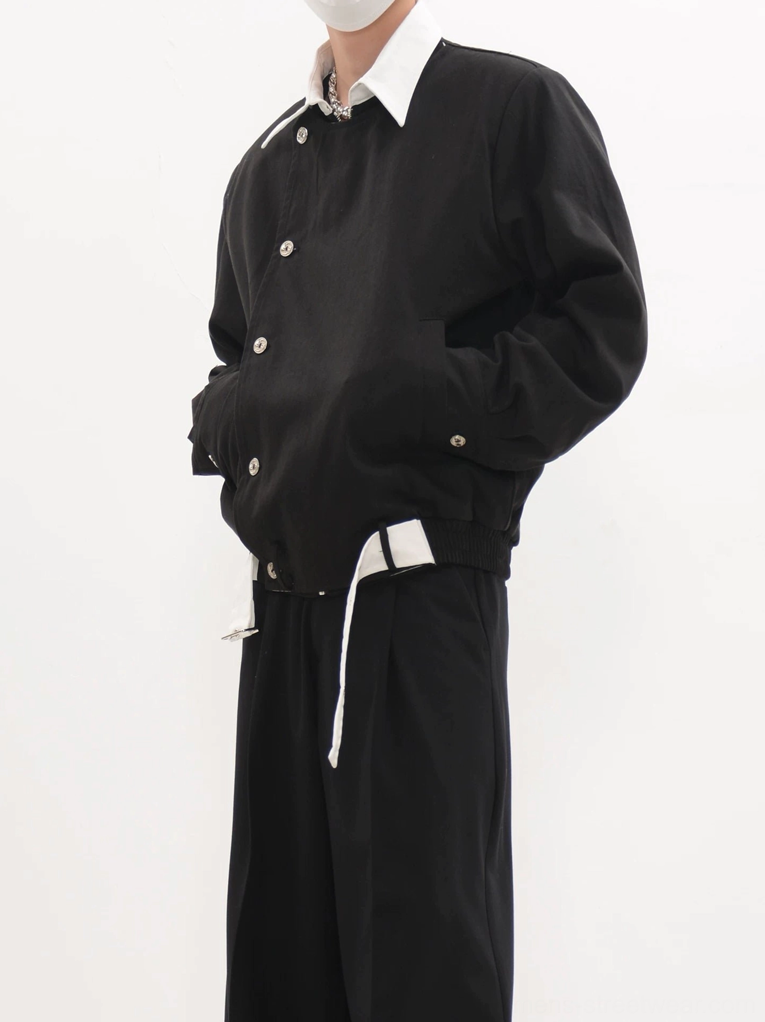 Black asymmetric button cropped blouson jacket worn with a white collared shirt and black wide-leg trousers in a studio