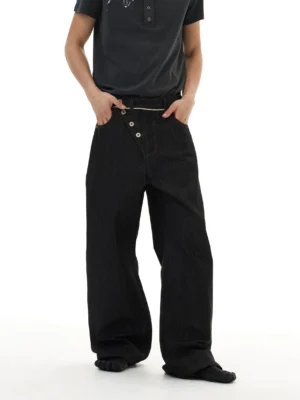 Male model wearing relaxed baggy wide-leg black denim jeans with an asymmetric button closure in Korean streetwear style