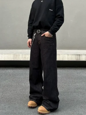 Three-quarter view of men's baggy washed black wide-leg jeans with a pocket chain styled with wheat-colored work boots for an urban streetwear outfit