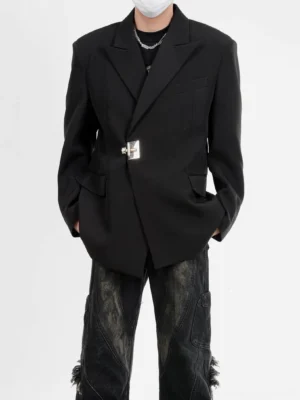 Front full-body view of a men's black asymmetric latch blazer with oversized padded shoulders, silver metal closure, notch lapels, black tee, silver necklace, and distressed wide-leg jeans