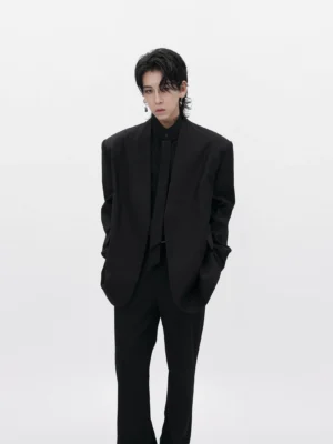 Men wearing a black collarless oversized minimalist blazer with matching black tailored trousers in a white studio
