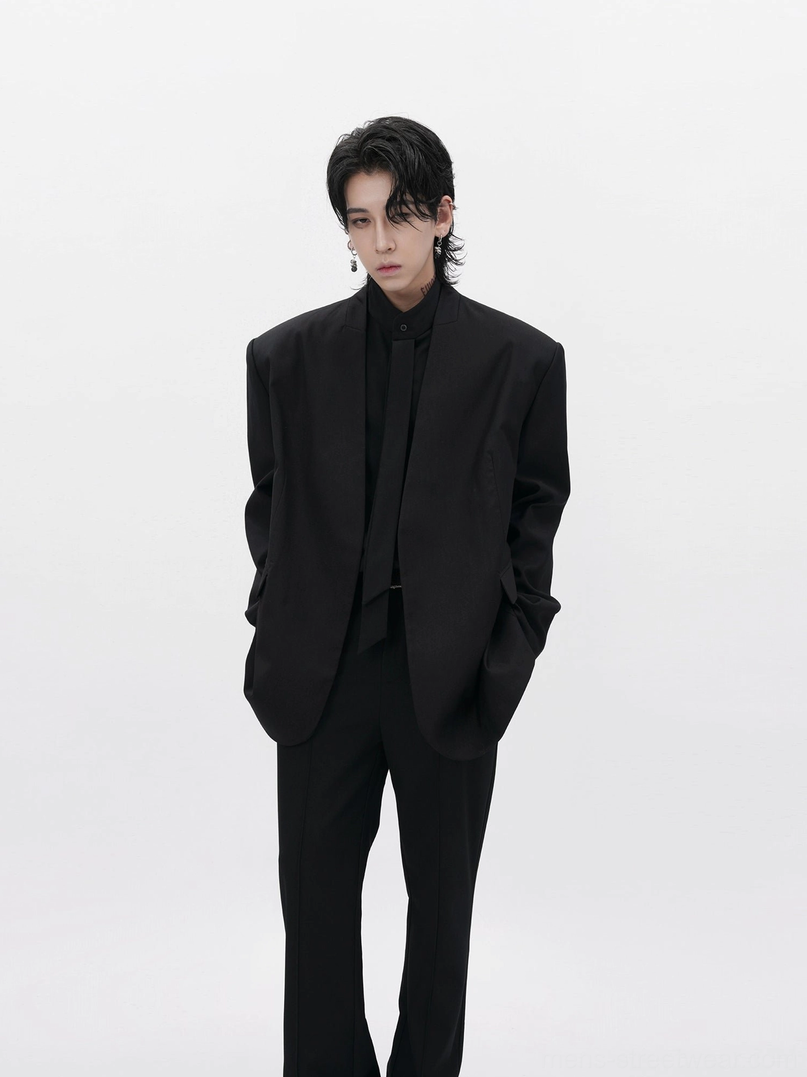 Men wearing a black collarless oversized minimalist blazer with matching black tailored trousers in a white studio