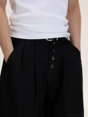 Close-up of men's black culottes waist showing four-button front placket, pleated tailoring, leather belt, and side pockets