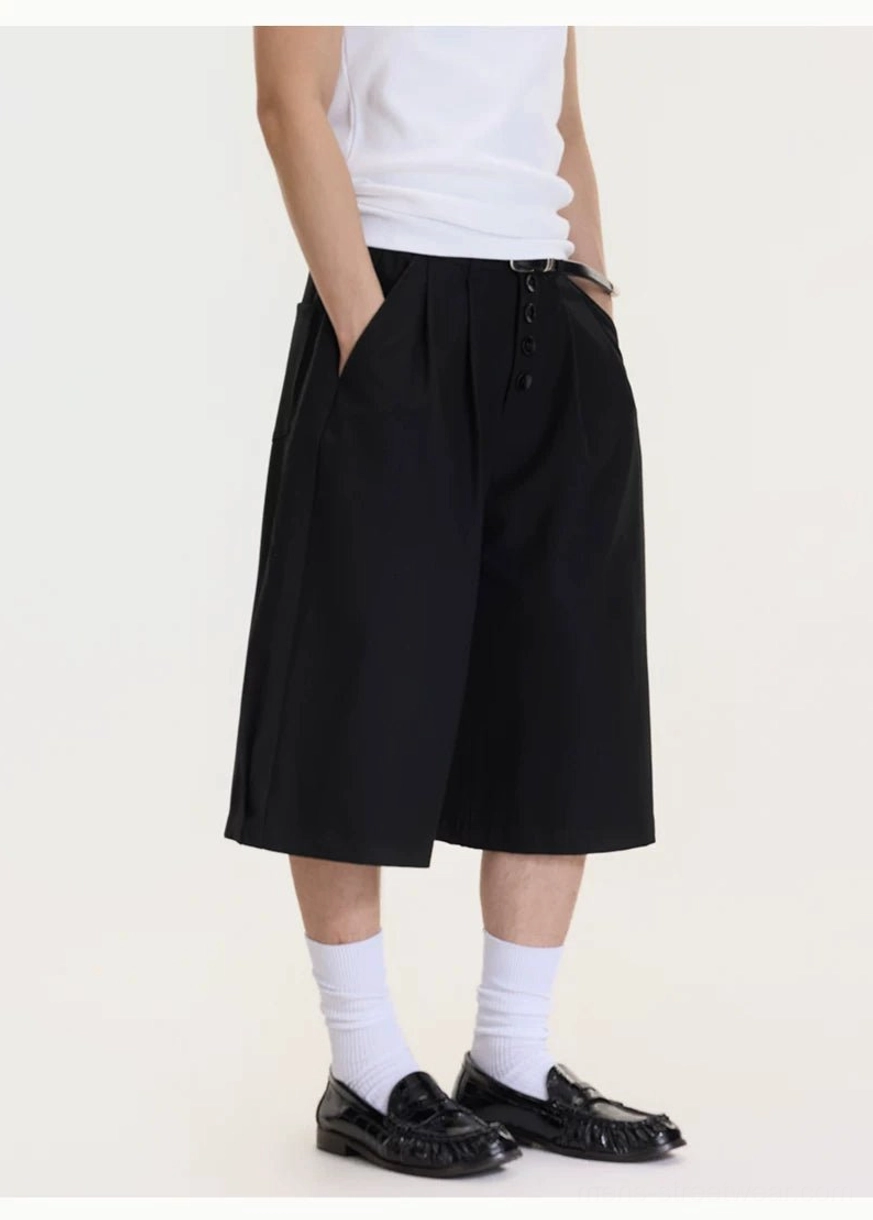 Three-quarter view of men's black drop-crotch culottes showing relaxed drape, wide legs, front buttons, and side pocket styling