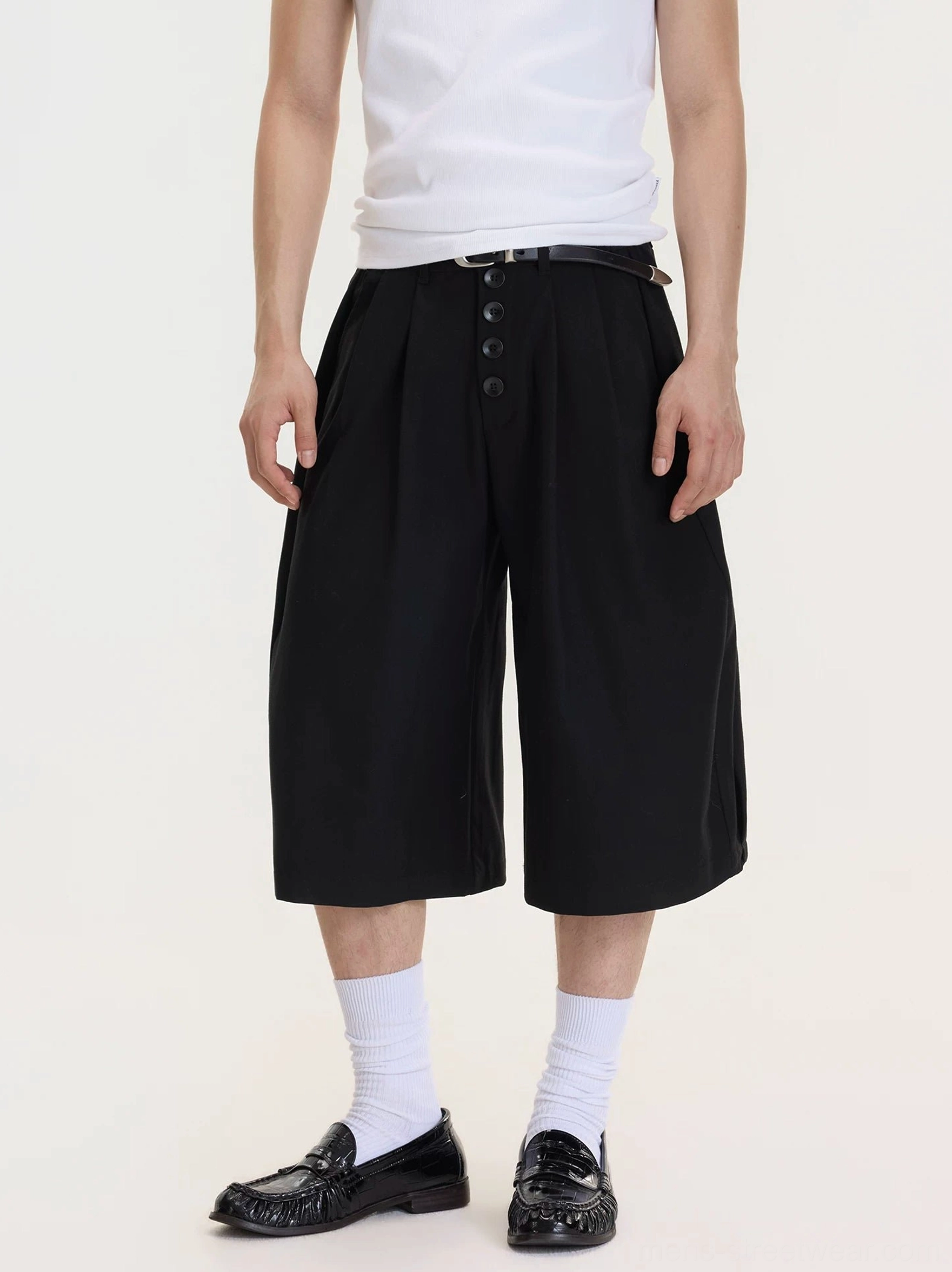 Front full-body view of men's black drop-crotch wide-leg culottes styled with a white tank top, white crew socks, and black leather loafers