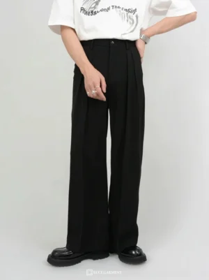 Men wearing black high-waist pleated wide-leg tailored trousers with a white graphic T-shirt and black platform shoes in a studio