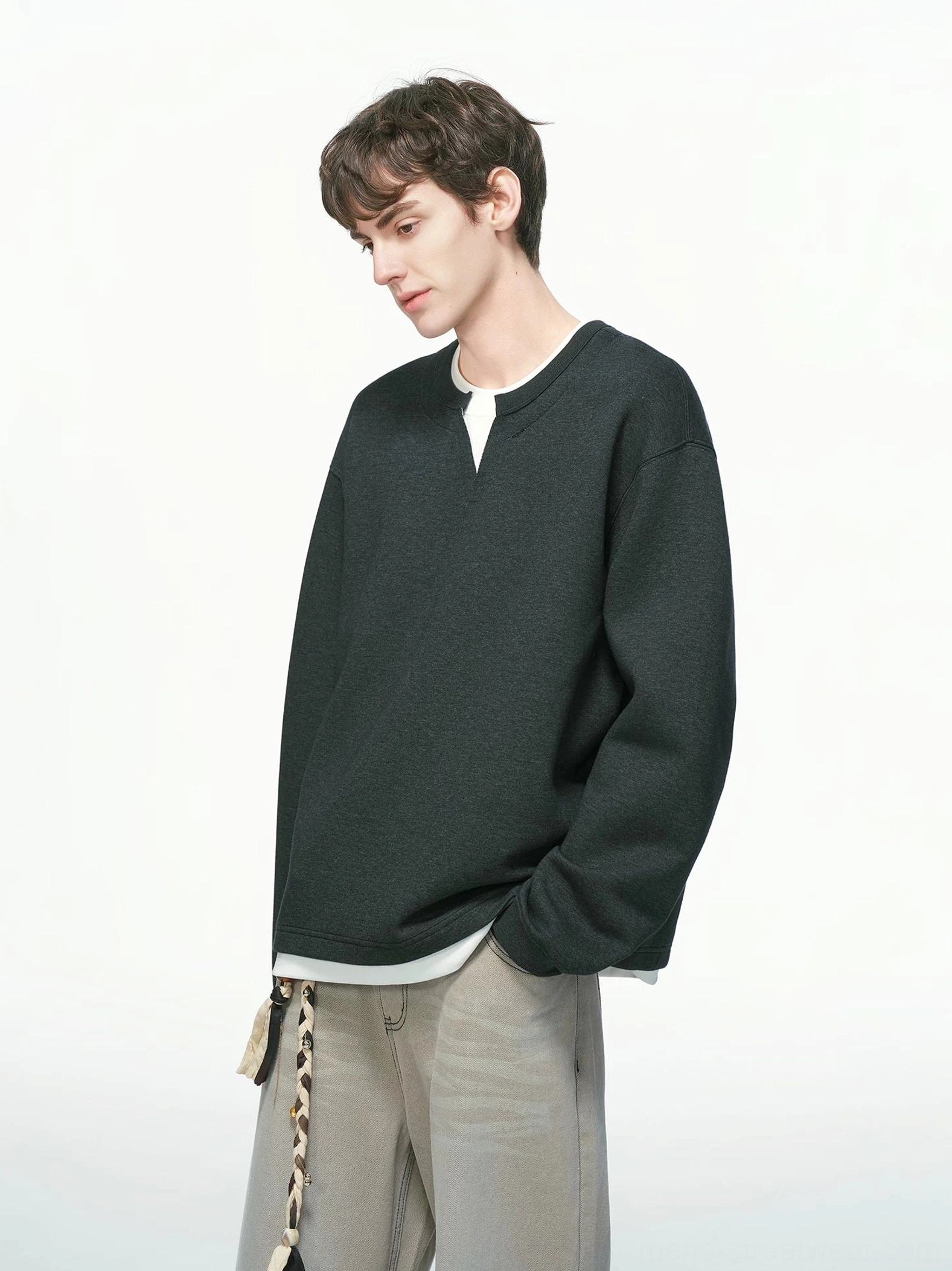 Black men's layered crew neck sweatshirt shown from the left side with oversized relaxed fit and faux white undershirt hem, styled with loose khaki trousers