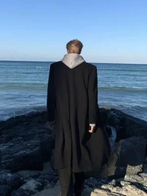 Back view of men's black layered hooded longline streetwear coat with exposed gray hood detail