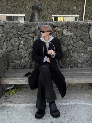 Men's black layered hooded longline streetwear coat worn in a seated front three-quarter outfit view