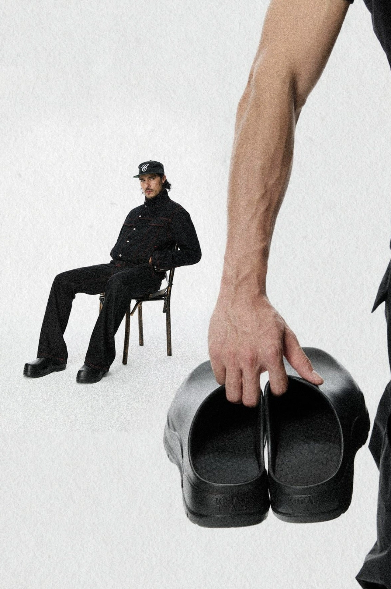 Male model wearing black platform clogs with an all-black streetwear outfit in a minimalist studio fashion setting
