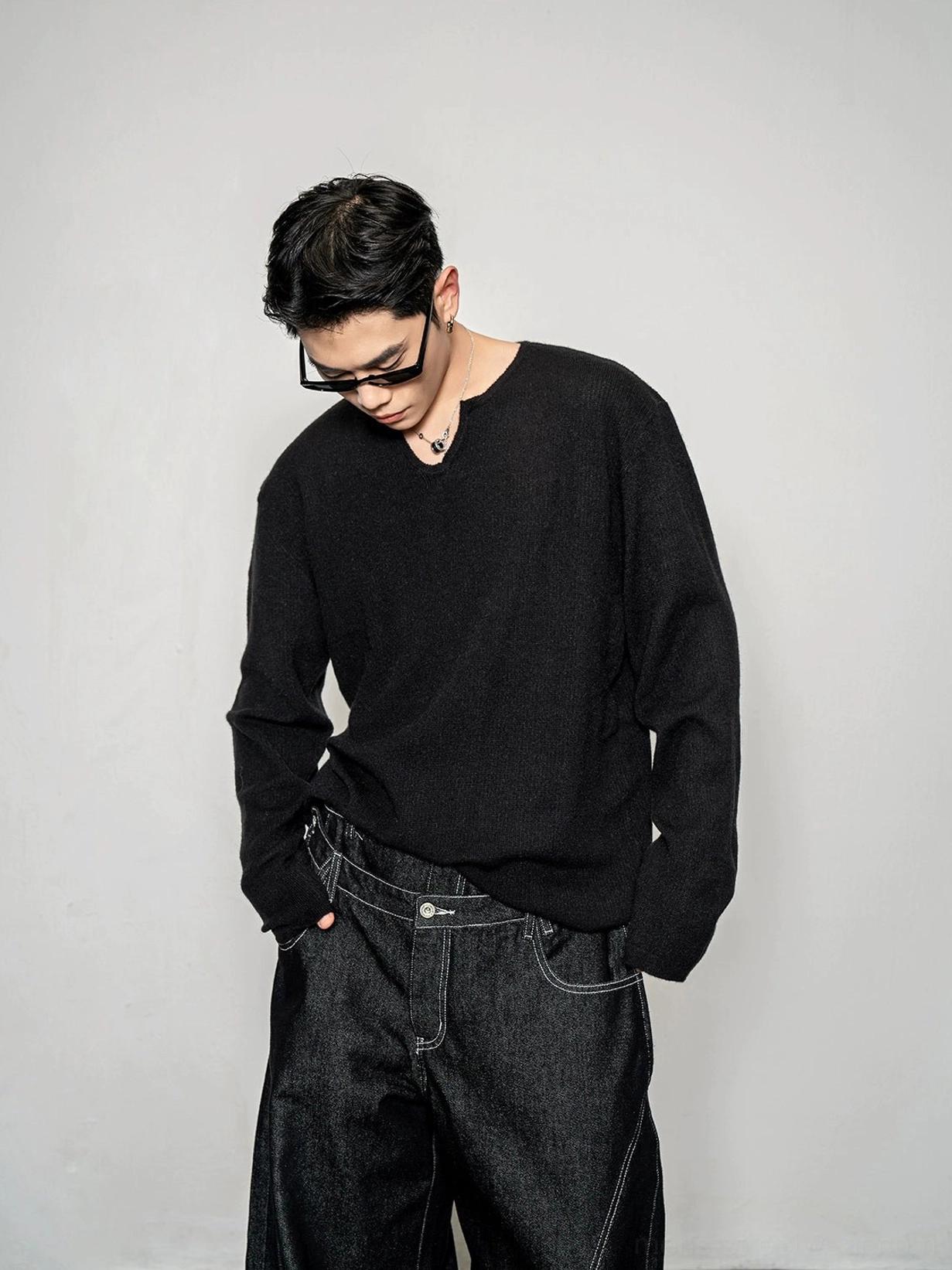 Black men's relaxed notch neck knit sweater styled with dark wide leg denim in a minimalist Seoul streetwear studio look