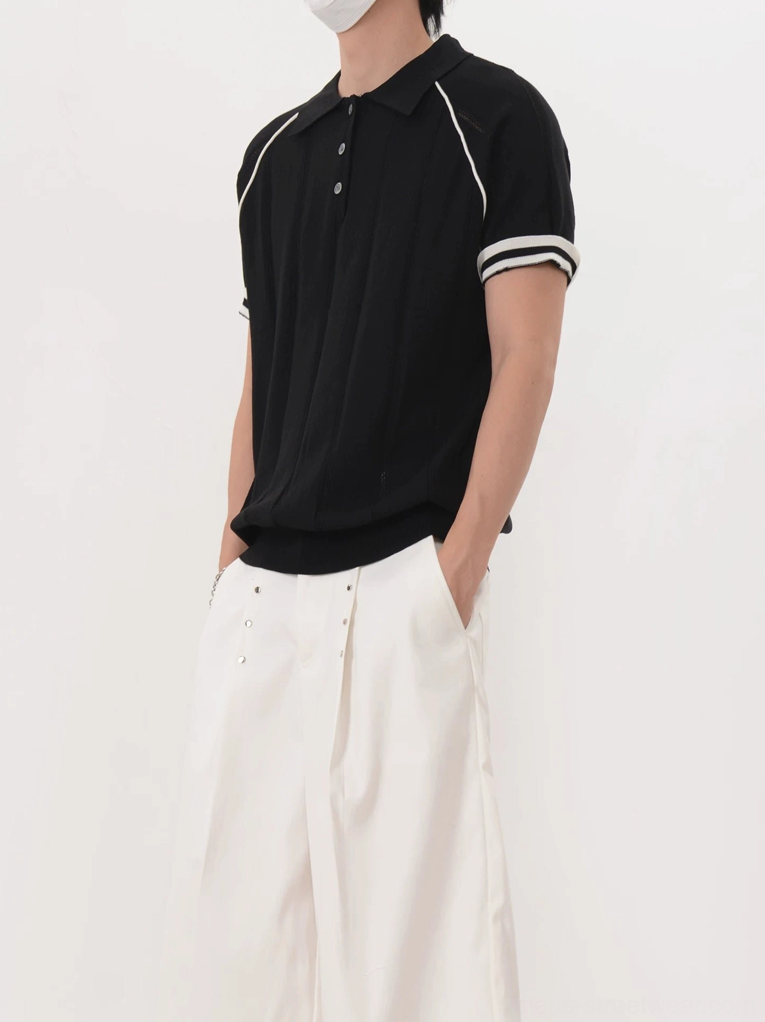 Men's black retro contrast trim ribbed knit polo shirt left side view with white wide-leg pants
